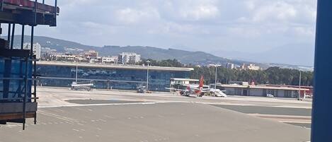 Una pista de aeropuerto con aviones estacionados, una torre de control y edificios a lo lejos.