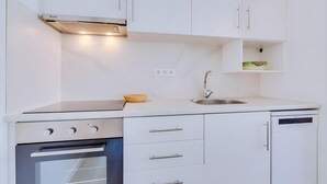 Cozinha moderna com armários brancos, forno embutido, lava-louças e torneira de aço inoxidável.