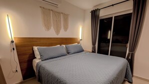 Ein Schlafzimmer mit einem großen Bett, einem Holz-Kopfteil, Wandleuchten und einer Schiebeglastür.