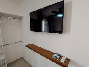 A room with a mounted TV, a wooden shelf with a remote, and a white closet with hanging clothes. - [4] beach & central near studio w/ sunny garden (Cancún)