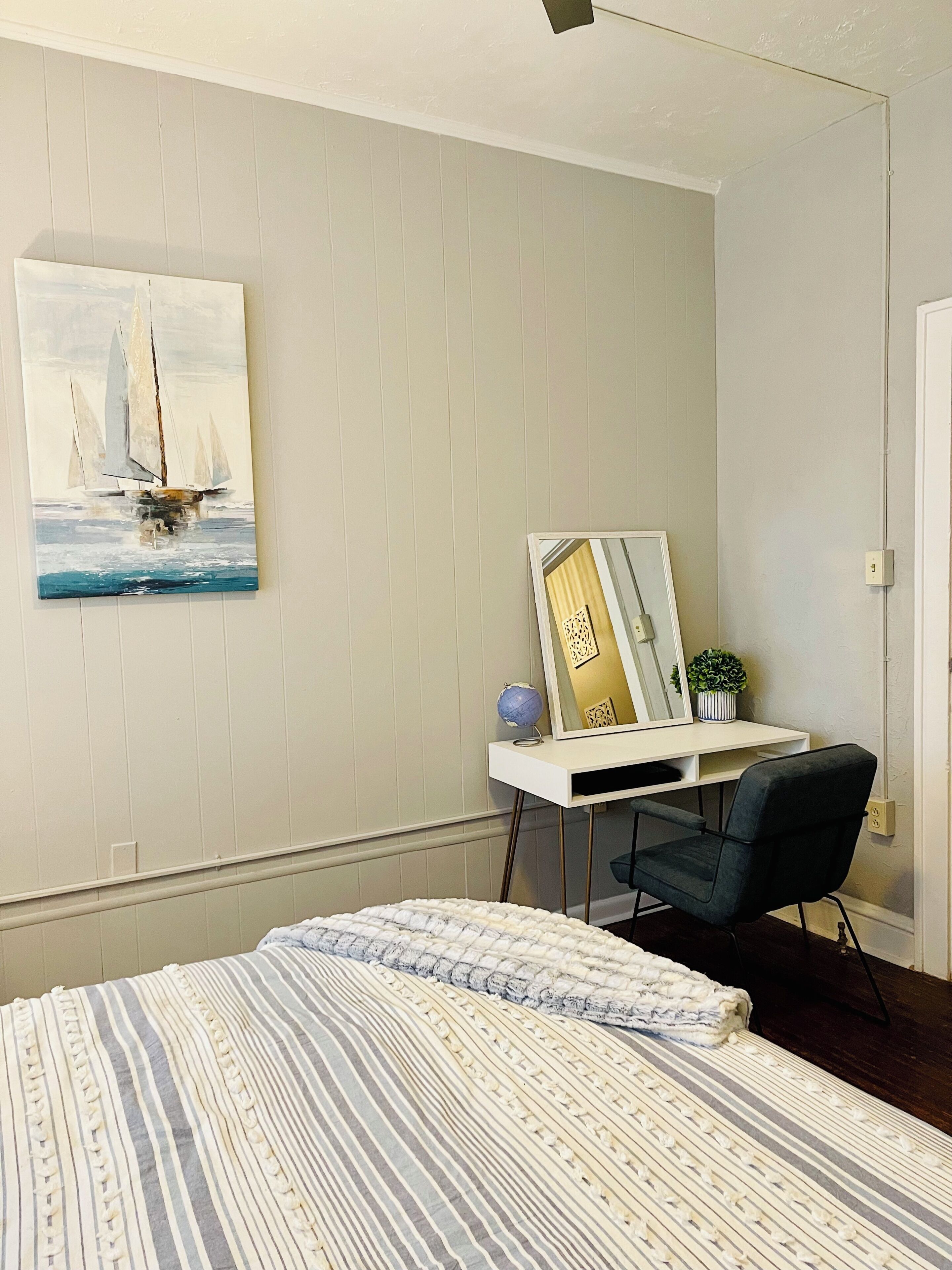 A bedroom with a bed, a desk with a chair, a painting, and a globe.