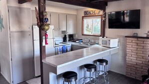 Una cocina moderna con una isla central, taburetes de bar, estufa, microondas y un televisor montado en la pared.