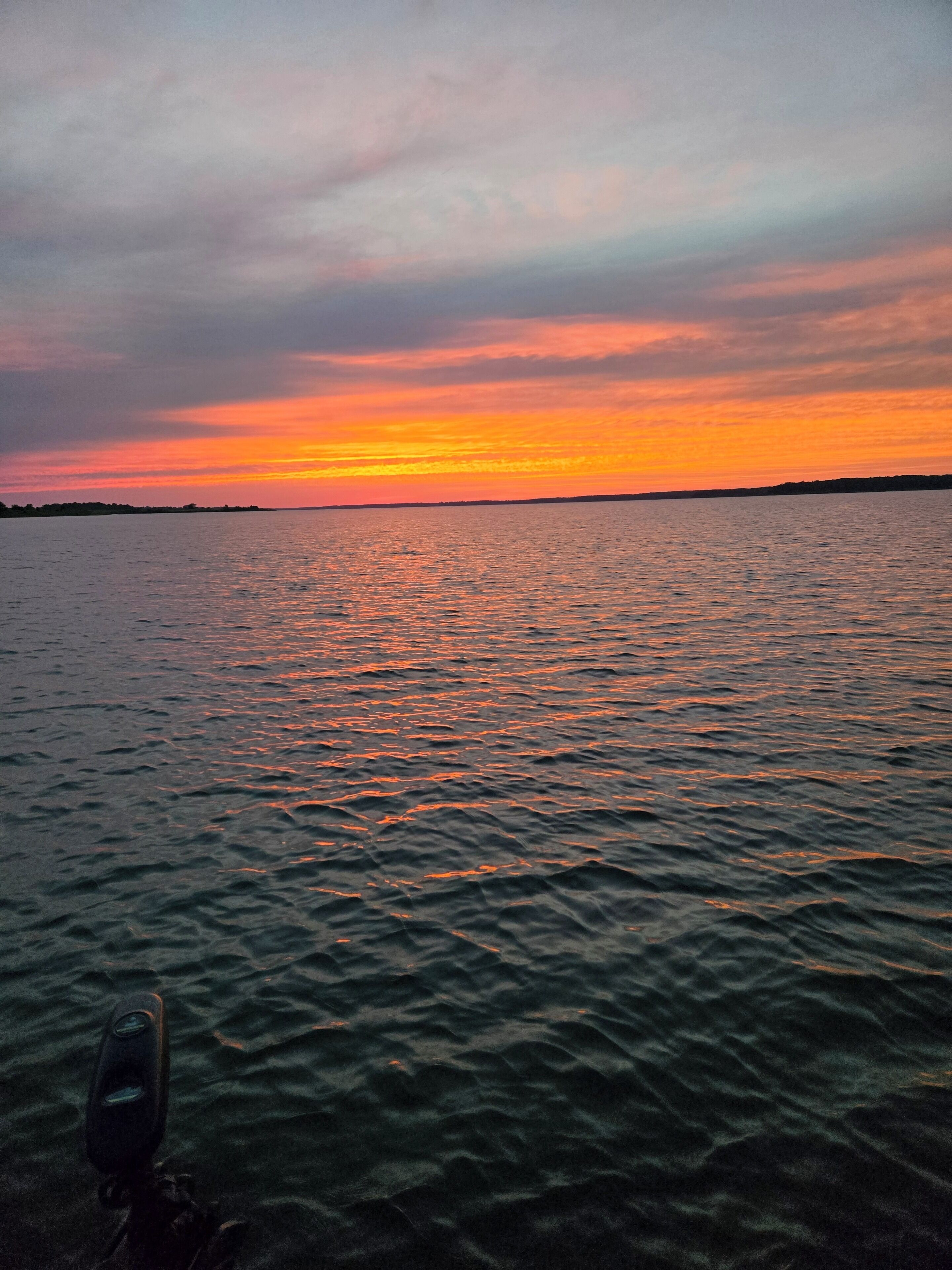 A sunset over a body of water with a silhouette of land in the distance.