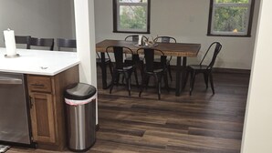 Un comedor con mesa y sillas de madera, un cubo de basura y un refrigerador.