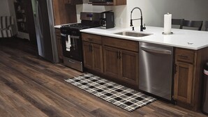 Una cocina con armarios de madera, electrodomésticos de acero inoxidable, una encimera blanca y una alfombra estampada.