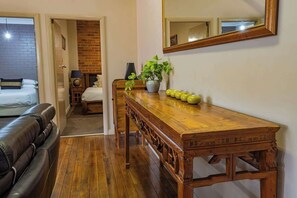 Una habitación con una mesa de comedor de madera, una planta en maceta, un espejo y una cama frente a una pared de ladrillo.