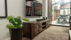 A modern office space with a large flat-screen TV mounted on the wall, a wooden desk with drawers, and a large potted plant. - Newcastle CBD Penthouse (Newcastle West)