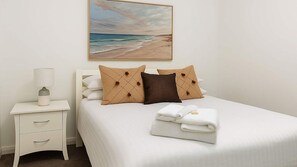 A hotel room with a bed, a nightstand, a lamp, and a painting of a beach scene. - Newcastle CBD Penthouse (Newcastle West)