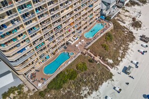 Ein Hochhaus-Hotel mit zahlreichen Balkonen, einem zentral gelegenen Schwimmpool und einer Strandanlage.