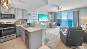 A modern kitchen with a built-in microwave, stove, and sink. There is a large flat-screen TV mounted on the wall. - Seychelles 1207 (Panama City Beach)