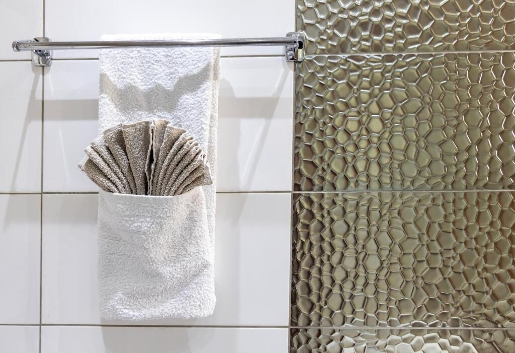 A bathroom with a white tiled wall, a towel rack with a white towel and a folded towel, and a textured wall with a honeycomb pattern.