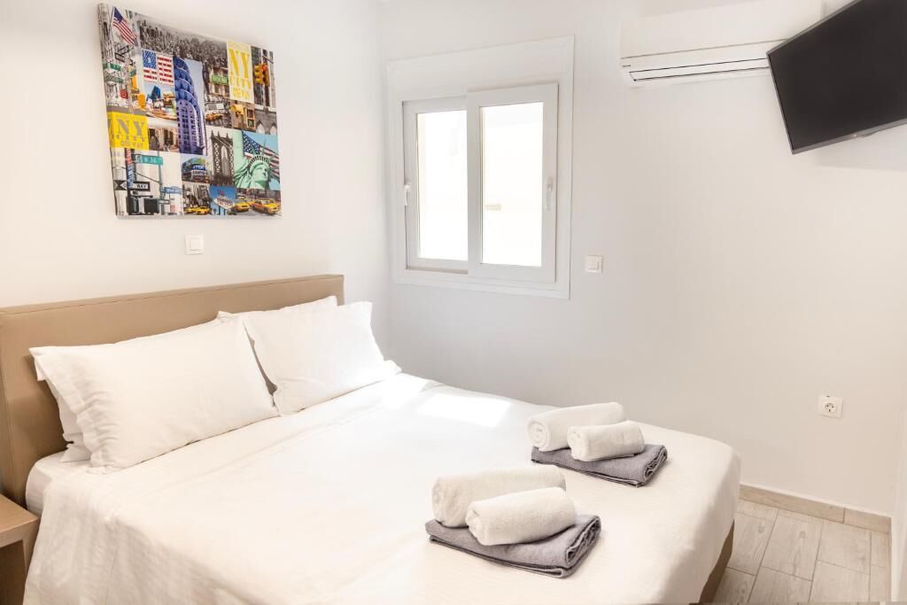 Ett hotellrum med en säng, kuddar, en tv som är monterad på väggen och ett fönster.