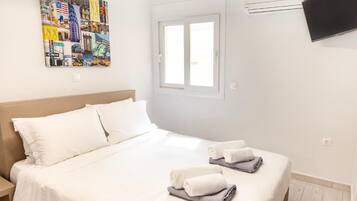 Ett hotellrum med en säng, kuddar, en tv som är monterad på väggen och ett fönster.