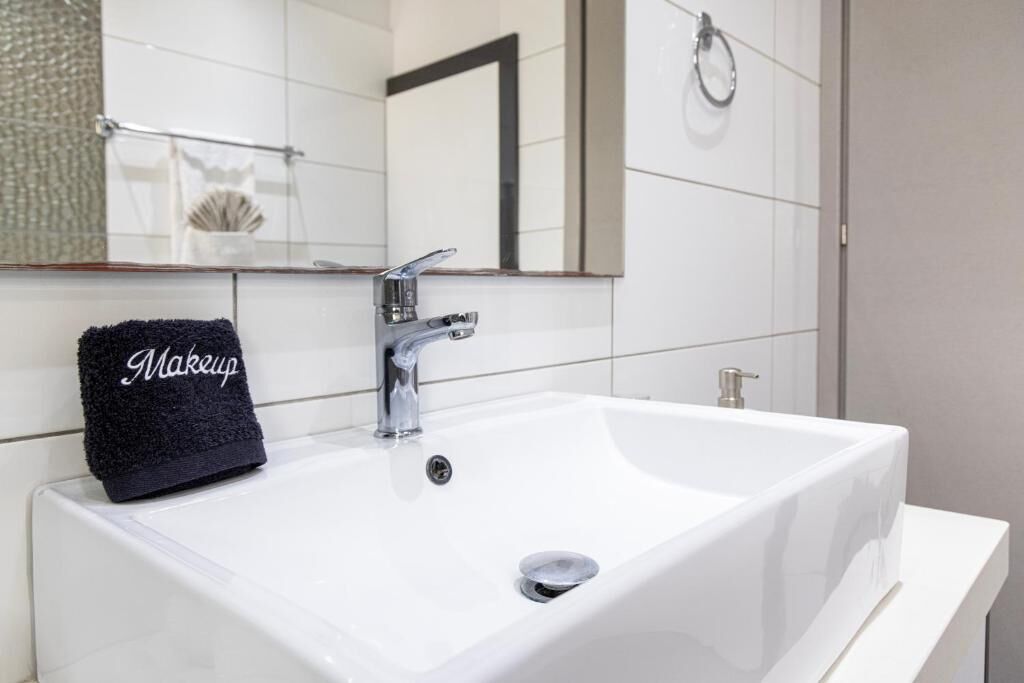 A white bathroom sink with a chrome faucet, a black towel with 'Makeup' written on it, and a mirror above the sink.