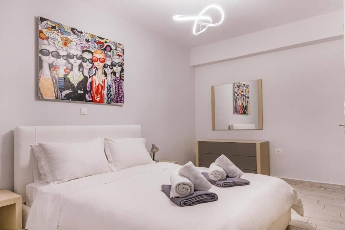 Una habitación de hotel con una cama grande, cabecero, mesita de noche, espejo y un cuadro colgado en la pared.
