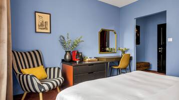 A hotel room with a bed, a desk, a chair, a dresser, a mirror, and a framed picture on the wall.