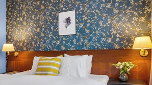 A neatly made bed with white and yellow striped pillows, a framed artwork above it, and a nightstand with a vase of flowers. - Penzion V Holi (Průhonice)