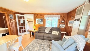 Ein gemütliches Zimmer mit einer Couch, einem Esstisch, Stühlen, Holzwänden und einem Fenster mit Aussicht.