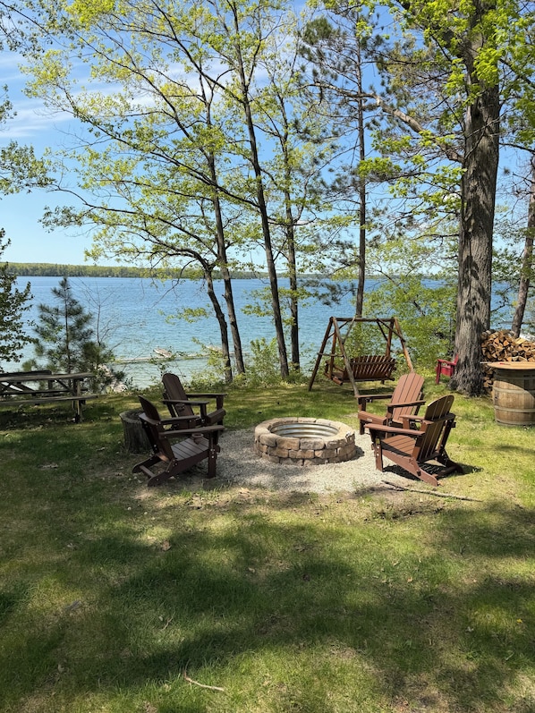 Ein Campingplatz am Seeufer mit Adirondack-Stühlen, einer Feuerstelle und einem Picknicktisch.