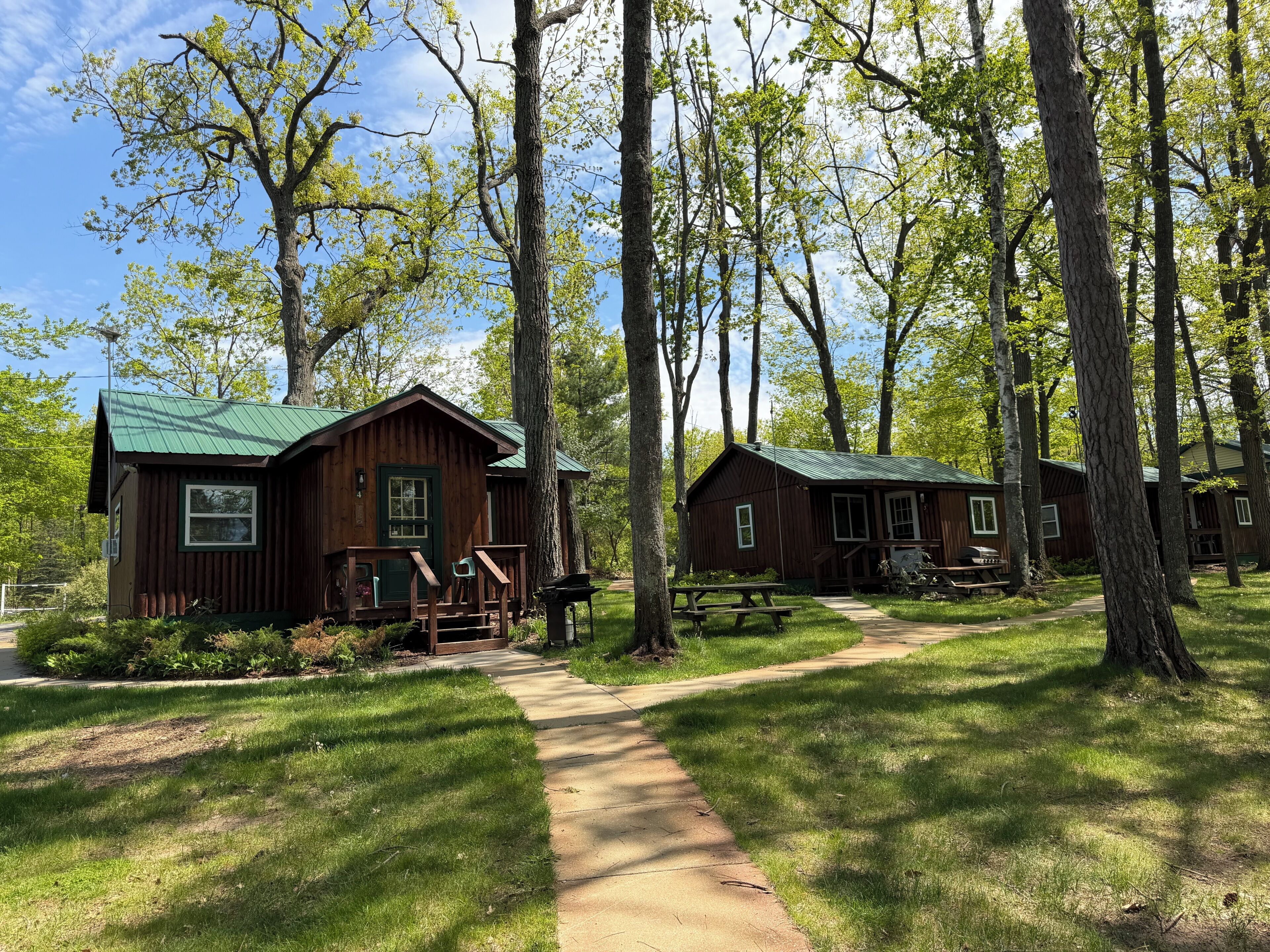 A rustic cabin-style lodging area with multiple wooden cabins, a paved walkway, and surrounding greenery.