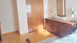 Une chambre à coucher avec une armoire en bois, une commode avec des lampes, un miroir et une couvre-lit à motifs.