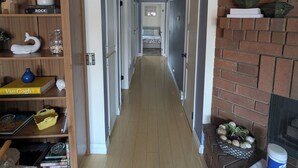 Un couloir avec une bibliothèque en bois, une cheminée en briques et un lit visible au loin.