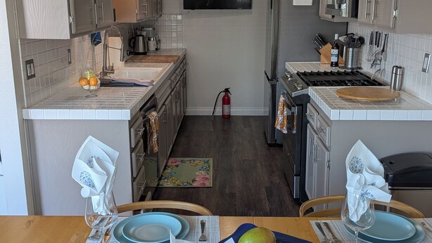 Une cuisine avec un îlot central, une table à manger avec des chaises et un téléviseur fixé au mur.