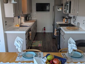 A kitchen with a central island, a dining table with chairs, and a TV mounted on the wall. - Charming 2-bedroom condo Near Disneyland and Beaches (Orange)