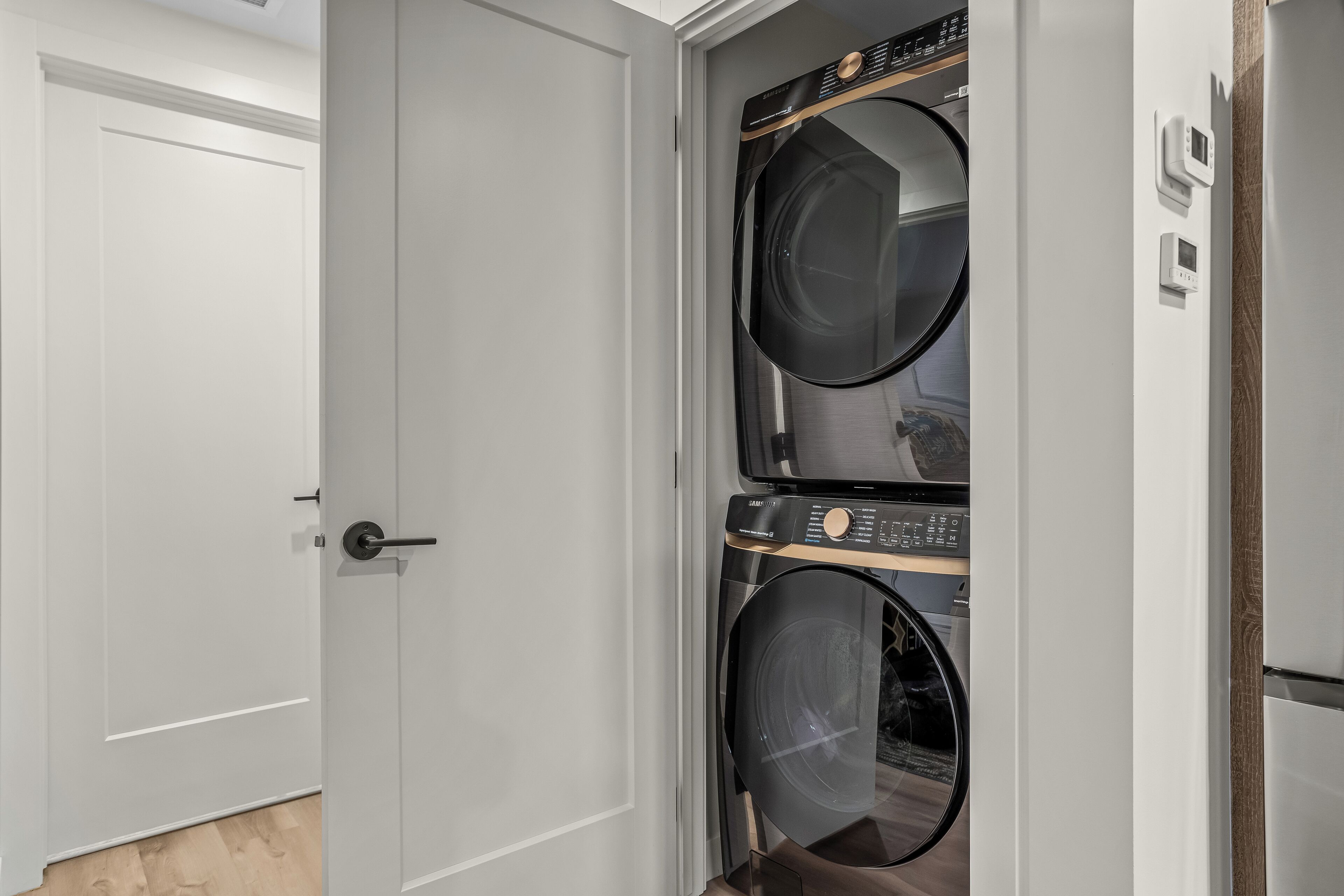 A laundry room with a door, two stacked washers and dryers, and a thermostat on the wall.