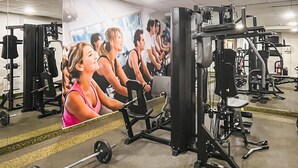 A gym with exercise equipment, a bench, and a mirror reflecting the room.