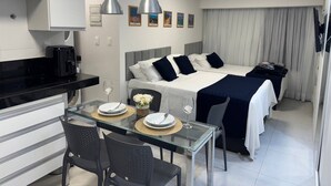 Une chambre d’hôtel moderne comprenant un lit, un coin repas avec une table en verre et une kitchenette.