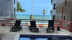 A swimming pool with lounge chairs, a view of the beach, and a tall structure in the background.