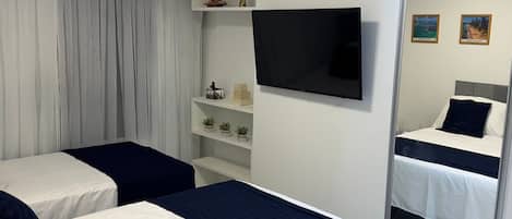 Habitación de hotel con dos camas, un televisor de pantalla plana, un estante con objetos decorativos y una ventana con cortinas.