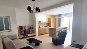 Uma sala de estar moderna com sofá, mesa de centro, televisão e área de cozinha com armários de madeira e balcão.