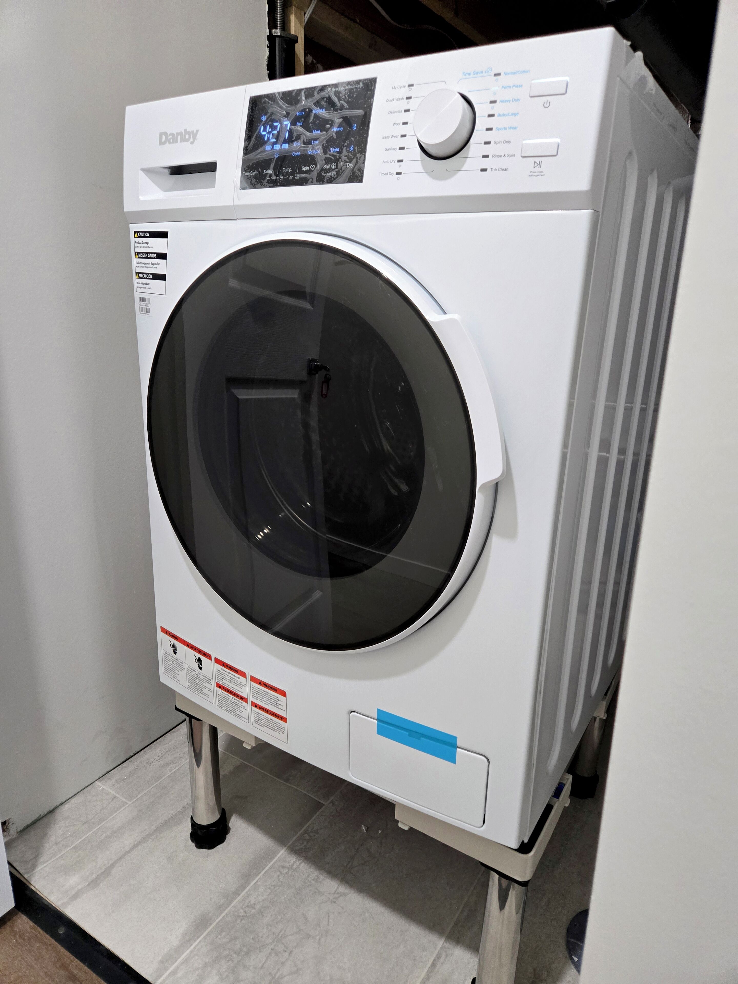 A white Danby front-loading washing machine with a digital display, control panel, and safety labels.