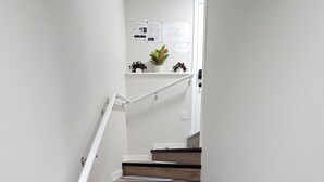 A staircase with wooden steps and white handrails, leading to a landing with a white wall and some plants. - Stylish New 2BR Suite | Private Entry | Quiet, Near Shops & Transit (Winnipeg)
