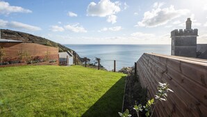 A coastal property with a grassy yard, a wooden deck, and a stone tower. - Cornica - Pet Friendly Coastal House with Hot Tub and Sea Views (Portwrinkle)