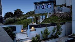 A modern building with a unique circular window design, a staircase leading to a higher level, and a well-maintained garden area. - Cornica - Pet Friendly Coastal House with Hot Tub and Sea Views (Portwrinkle)