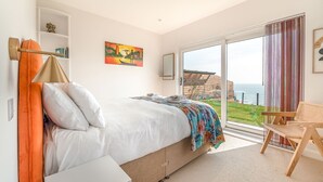 A bedroom with a bed, a chair, a large window, and a painting on the wall. - Cornica - Pet Friendly Coastal House with Hot Tub and Sea Views (Portwrinkle)
