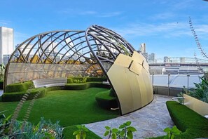 A modern architectural structure with a glass dome and a golden sculpture, surrounded by green landscaping and a view of a stadium. - Level 69 Bay Views & Japanese Soaking Tub (Melbourne)