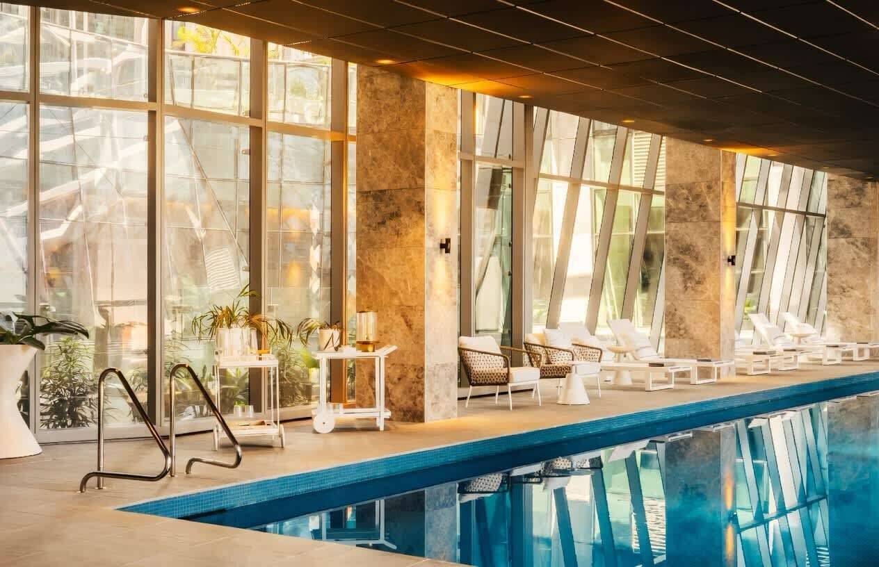 Ein überdachter Pool mit großen Glaswänden, Liegestühlen und hellem Tageslicht.