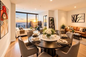 A modern dining room with a round table set for six, large windows offering a city view, and a cozy living area with a sofa and a coffee table. - Level 69 Bay Views & Japanese Soaking Tub (Melbourne)