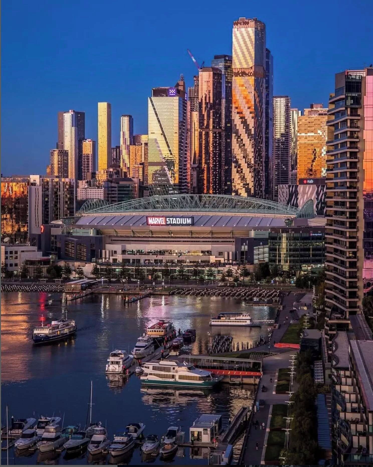 A waterfront view of a city skyline with a prominent stadium labeled 'Marvel Stadium' in the foreground.