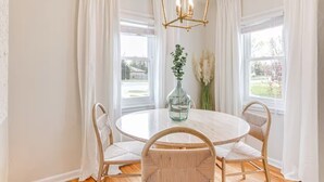 Un coin repas comprenant une table ronde, quatre chaises, un vase avec des plantes et un lustre aux motifs géométriques.
