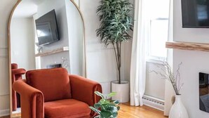 Un salon avec une table basse ronde en marbre, un fauteuil rouge, un grand miroir, une plante en pot et une cheminée.