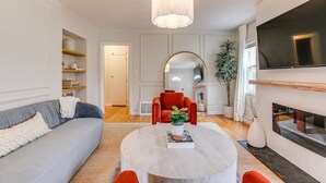 Un salon moderne avec un canapé, une table basse ronde, un fauteuil rouge, un téléviseur et une cheminée.