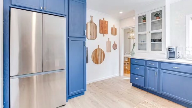 Une cuisine moderne avec des meubles bleus, un réfrigérateur en acier inoxydable, des éléments de décoration en bois sur les murs et une vue sur la salle à manger.
