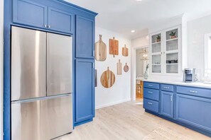 Eine moderne Küche mit blauen Schränken, einem Edelstahlkühlschrank, Holzverzierungen an der Wand und Blick in den Essbereich.