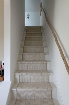 A staircase with a herringbone carpet pattern, white walls, and a wooden handrail. - Designer Waterfront Newly Renovated Cottage "ROXABOXEN" (Tremont)