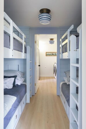 Un couloir étroit, avec des lits superposés de chaque côté, une porte au fond et un luminaire au plafond.
